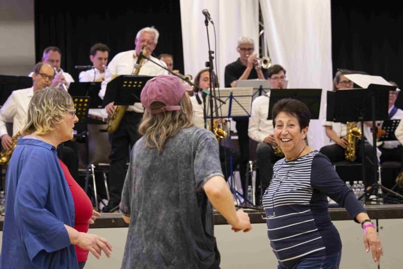 3 Personen tanzen vor einer spielenden Bigband.